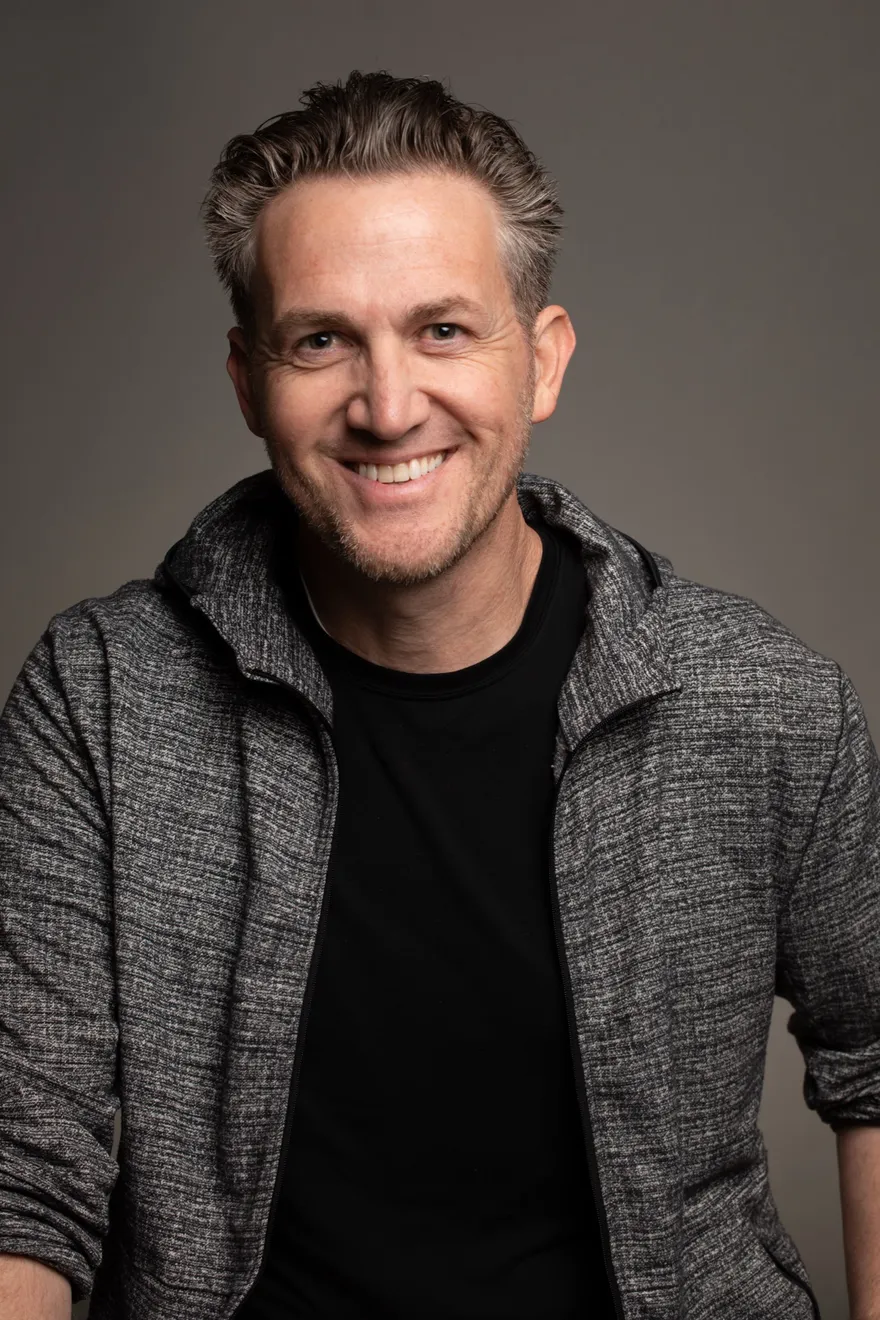 Matthew Dearing, 2025. Grey hoodie, warm smile, grey studio backdrop.